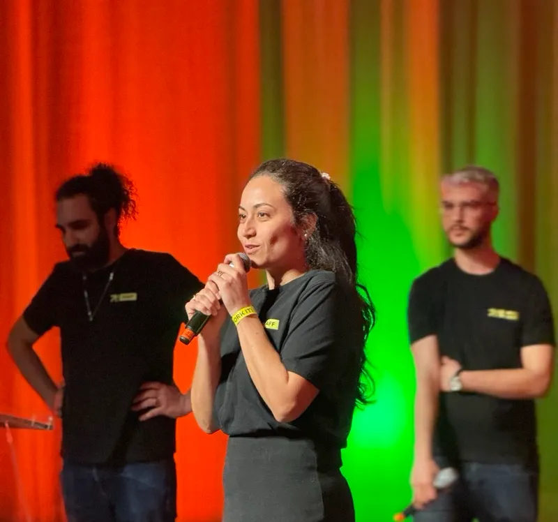 Hend Fellah speaking in front of the attendees. We can see Yoann Fleury, and Aziz Ouertani behind her